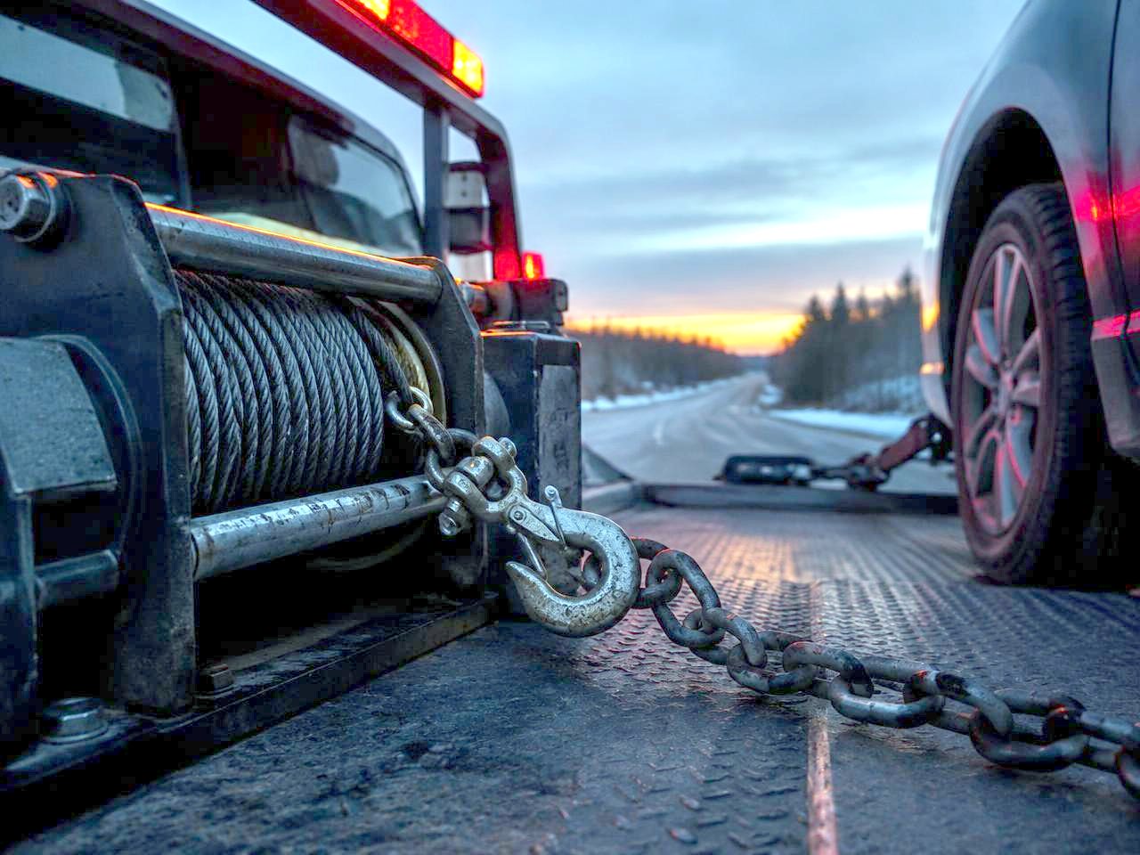 Close-up of a flatbed tow truck winch and chain securing a vehicle at dusk