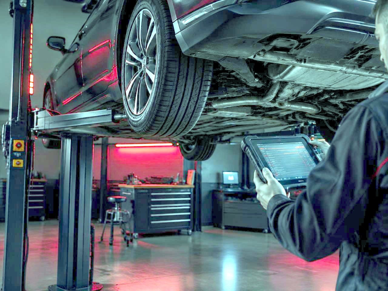 Car raised on a lift while a technician reviews a diagnostic tablet